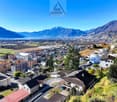 Aerial view of houses on hillside with lake, mountains, and a city in the background.