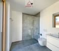 modern bathroom with gray tiles, glass shower enclosure, white vanity, toilet, silver faucet
