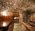 Stone walls, wooden tables, benches, wine racks, metal wine storage, a small arch window
