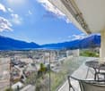 balcony with table and chairs, glass railing, mountain view, city view, clear blue sky, white clouds