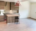modern kitchen with white walls, wooden floor, kitchen island with a black stool, wooden cabinets, oven, sink, window, tiled backsplash