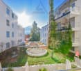 White modern building, multiple floors, multiple balconies, a garden with plants and rocks