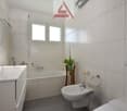 Bathroom with white tiles, bathtub, sink, toilet, bidet, mirror, potted plant, and a window.