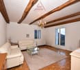 living room with white leather couches, glass coffee table, wooden floor, wooden beams, chandelier, windows, radiator, rug