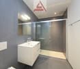 modern bathroom with white sink, mirror, glass shower enclosure, and gray tiles