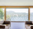 Large windows with a scenic mountain view, wooden frame, brown sofas, ornate metal railing on the balcony