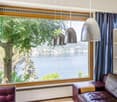 Large window with a scenic view of a lake surrounded by trees, leather sofa, pendant lighting fixtures, wooden window frame