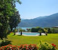 lakefront villa, pool in garden, greenery, mountains in background, patio area with garden furniture, decorative flowers