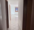 Long hallway, square tiles, white walls, ceiling light, windows with frames, doors on both sides