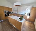 modern kitchen with wooden cabinets, white countertops, integrated oven, microwave, coffee machine, sink, plants
