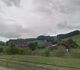 Houses in a rural area, surrounded by trees and grass, cloudy sky, a car parked on the side of the road