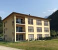 yellow three story building, 4 balconies, large grass field, mountain in the background
