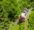 Stone house, rustic design, gable roof, surrounded by lush greenery, flag, pathway