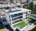 white apartment building, solar panels on the roof, multiple terraces, surrounded by other buildings