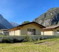 Row of small houses with beige and yellow walls, black roofs, double glass doors and windows, fenced in with plants, mountains in the background