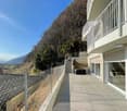A two story house with a balcony, tiled pathway, chain link fence, and stairs leading to a staircase with handrails.