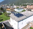 White building, Solar panels on the roof, several houses in the background, mountains