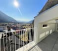 White building exterior, balcony with white railing, wooden deck flooring, view of the city and mountains