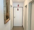 White walls, tiled floor, an entrance door, a picture frame on the left wall, and a small ornament hanging above the door.