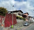 House with red leaves, stone wall, stairs leading to entrance, balcony, car parked on street