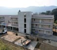 A multi-story building with balconies, under construction, surrounded by trees and mountains