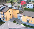 Aerial view of a group of houses, yellow and white, with balconies and terraces, surrounded by greenery and a mountain in the background