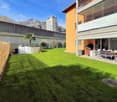 green lawn, wooden fence, palm tree, outdoor dining set, storage boxes, orange building with balcony