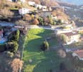 Aerial view of a hillside neighborhood with several houses, a large grassy field, and a road.