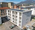 Aerial view of a modern apartment building with solar panels on the roof, balconies, and a parking area in front.