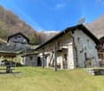 Stone house, solar panels on the roof, wooden porch, wooden ladder, garden, mountains in the background