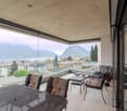 modern balcony with table, chairs, large glass windows, stunning lake and mountain view