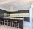Island with stools, modern cabinets, appliances, marble countertops, and recessed lighting.