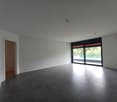 Large open space with white walls, gray tile flooring, and a sliding glass door leading to an outdoor area. The room appears to be empty, with no furniture or decor visible.