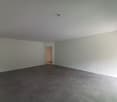 Large empty room with gray concrete flooring, white walls, and a doorway leading to another room.
