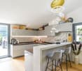 modern kitchen with large windows, marble countertop, breakfast bar, grey chairs, island with built-in appliances, plants, glass doors, balcony, chandelier