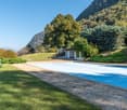 pool with concrete around, green benches, trees, bushes, grass, mountain
