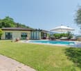 Villa with swimming pool, tiled roof, yellow exterior, garden, green lawn, trees, patio furniture