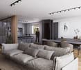 The image shows a modern, open-plan living space with a large, comfortable gray sofa, a dining area with a dark wooden table and chairs, and a kitchen area with sleek gray cabinets and countertops. The space is well-lit with track lighting and features la