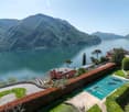 Luxury villa with a stunning view of the lake surrounded by mountains, with a swimming pool, balcony, and lush landscaping.