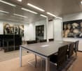 Modern office, large glass walls, wooden flooring, long table, black leather chairs, paintings on the wall