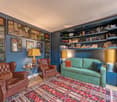 Living room with brown leather chairs, a green couch, a colorful carpet, side table, lamps, and a wooden floor