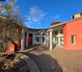 contemporary house with a red brick exterior, white pillars, large entrance, stone walkway, a flag on the rooftop, olive tree, and garden