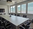 Conference room with a long table, multiple chairs, a mounted television, and large windows