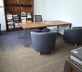 A modern office with a wooden desk, two black chairs, a bookshelf full of books, a potted plant, a radiator and gray office chair.
