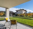 Terrace with chairs and cushions, green lawn, house in the background, mountains in the distance
