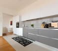 Modern kitchen with white cabinets, gray drawers, stainless steel appliances, and a decorative rug on the floor. The kitchen appears to be part of an open-concept living space with a view of other rooms in the home.
