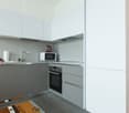 Modern, minimalist kitchen with gray cabinets, stainless steel appliances including a microwave and dishwasher, and a tiled floor.