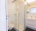 Bathroom with white tiles, shower cubicle, toilet, sink, cabinet, mirror, roll of toilet paper, and toilet paper holder.