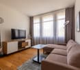 Spacious living room with large windows, hardwood flooring, beige sofa, TV stand, and decorative lamps