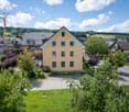 3 story house, light yellow exterior, multiple windows, surrounding greenery, driveway